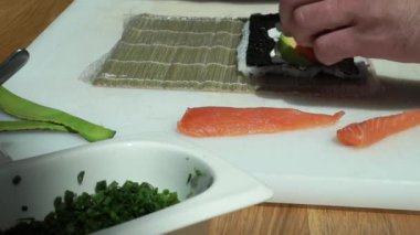 Suşi ustası Japon restoranında taze ve lezzetli suşi ruloları hazırlıyor ve tabağa koyuyor. Konsept: bambu matında suşi rulosu yapmak. Suşi yapmak, malzemeleri kesmek.