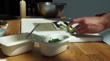 Suşi ustası Japon restoranında taze ve lezzetli suşi ruloları hazırlıyor ve tabağa koyuyor. Konsept: bambu matında suşi rulosu yapmak. Suşi yapmak, malzemeleri kesmek.