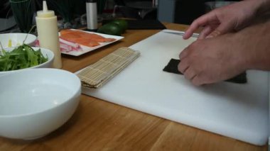 Suşi ustası Japon restoranında taze ve lezzetli suşi ruloları hazırlıyor ve tabağa koyuyor. Konsept: bambu matında suşi rulosu yapmak. Suşi yapmak, malzemeleri kesmek.