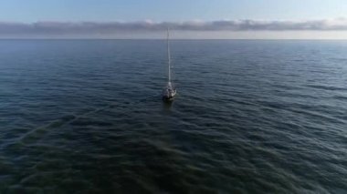 Güneşin doğuşundan sonra sakin denize açılan güzel yelkenli ya da yatın hava manzarası. Polonya 'da Baltık Denizi, yaz mevsimi. Denizin ortasında yalnız bir denizci.