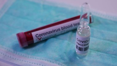 Coronavirus aşısı ve yeşil tıbbi maske üzerindeki kan testi yakından görülüyor. Konsept: COVID-2019 virüs koruması, Salgın, Wuhan virüsü ve dünya salgını, tedavi ve antibiyotikleri yayma