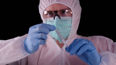 Coronavirus COVID-2019 aşı konsepti. Beyaz üniformalı, maskeli ve gözlüklü bir adam elinde Coronavirus aşısı olan şırıngalar tutuyor. Salgın için tedavi, salgını durdurmak, Wuhan 'dan virüs aşısı.