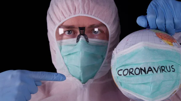Man in professional white safety uniform is showing globe with Coronavirus labeled mask. Concept: coronavirus Covid-19 epidemic. World pandemic.