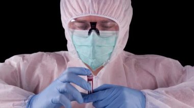 Profesyonel beyaz güvenlik üniformalı adam, biyotehlike etiketli pozitif Coronavirus kan testi yapan test tüpünü izliyor ve gösteriyor. Covid-19 salgını. Dünya salgını.