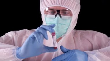 Profesyonel beyaz güvenlik üniformalı adam, biyotehlike etiketli pozitif Coronavirus kan testi yapan test tüpünü izliyor ve gösteriyor. Covid-19 salgını. Dünya salgını.