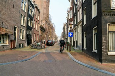 Yaşlı gri saçlı bir adam Amsterdam 'da dar bir sokakta tek başına bisiklet sürüyor.