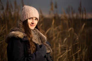 Ormanda hamile bir kadın ya da sonbaharda ya da kışın çimen. Çimlerin üzerinde duran bir kadının hamilelik fotoğrafı. Şapka ceketini soğuk giyer.