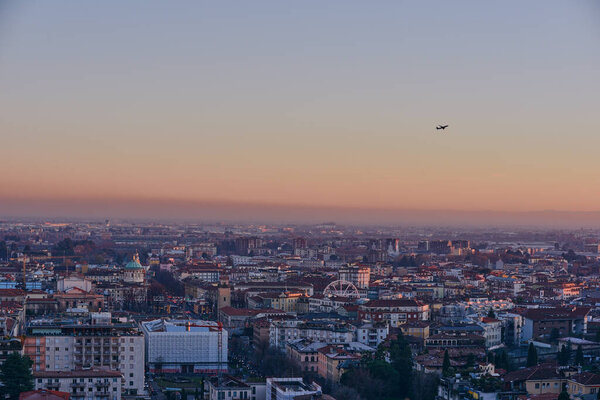 The view of the city of Bergamo at sunset from the walls of the upper city, with an airplane taking off