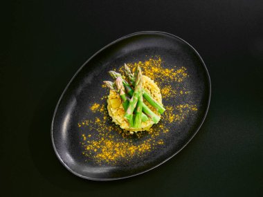 Ahşap bir masada siyah bir tabakta kuşkonmaz ve köri (tereyağsız) ile vegan risotto.