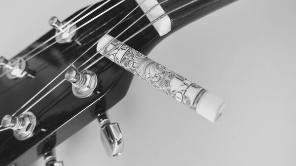Guitar headstock closeup and banknote rolled up with copy space . black and white