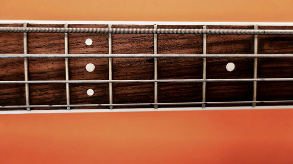 Bass guitar neck closeup . Copy space . Orange background