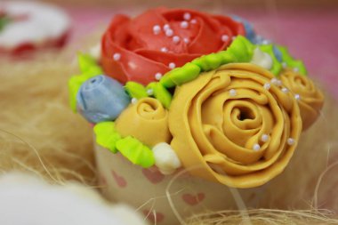 Pembe arka planda çiçeklerle süslenmiş lezzetli renkli kekler.