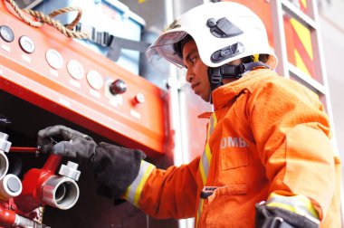 İtfaiye memuru tam teçhizatla itfaiye arabasının yanında duruyor.