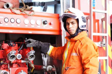 İtfaiye memuru tam teçhizatla itfaiye arabasının yanında duruyor.