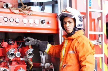 İtfaiye memuru tam teçhizatla itfaiye arabasının yanında duruyor.