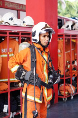 İtfaiye memuru tam teçhizatla itfaiye arabasının yanında duruyor.