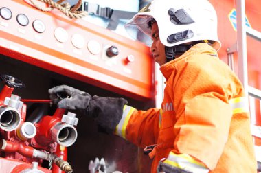 İtfaiye memuru tam teçhizatla itfaiye arabasının yanında duruyor.