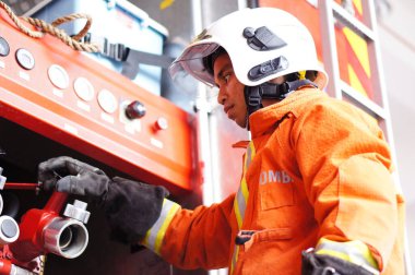 İtfaiye memuru tam teçhizatla itfaiye arabasının yanında duruyor.