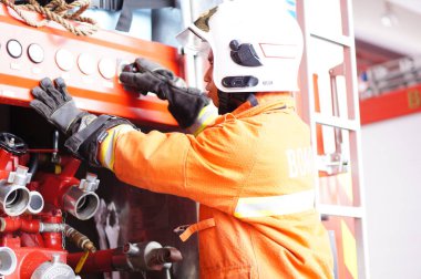 İtfaiye memuru tam teçhizatla itfaiye arabasının yanında duruyor.