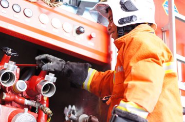 İtfaiye memuru tam teçhizatla itfaiye arabasının yanında duruyor.