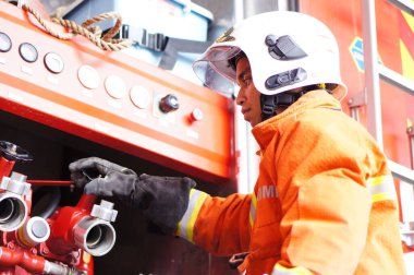 İtfaiye memuru tam teçhizatla itfaiye arabasının yanında duruyor.