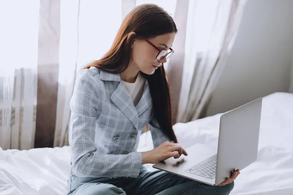Mujer en la cama durante el día trabajando con un ordenador portátil . — Foto de Stock