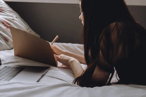 Fiatal nő fekszik az ágyban laptop és notebook. — Stock Fotó