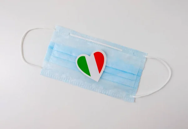Kalp şeklinde minyatür bir İtalya bayrağı taşıyan tıbbi koruyucu maske.. — Stok fotoğraf