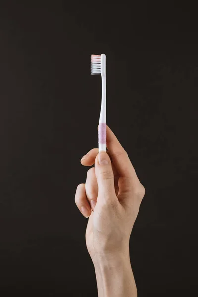 Female hand holds a toothbrush on a black background. — Stock Photo, Image