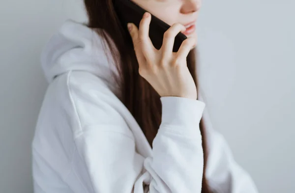 Femmina in una felpa bianca con cappuccio tiene uno smartphone . — Foto Stock