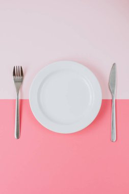 Pembe şeftali arka planında çatal bıçak takımı olan boş beyaz tabak..