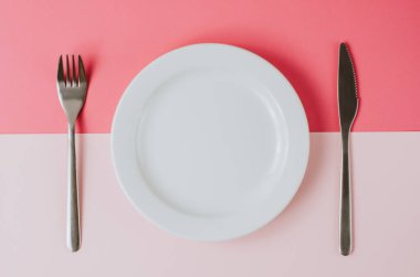 Pembe şeftali arka planında çatal bıçak takımı olan boş beyaz tabak..