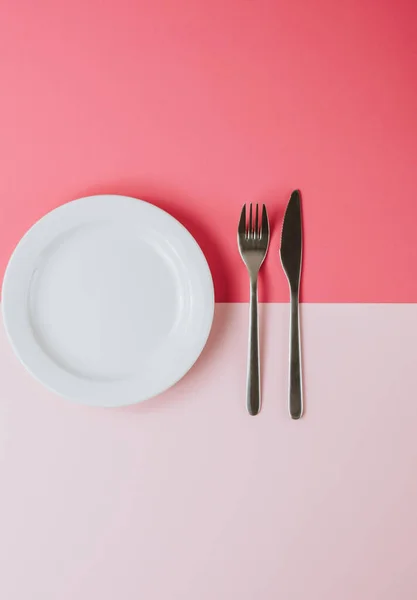 Placa blanca vacía con cubiertos sobre fondo rosa-melocotón . —  Fotos de Stock