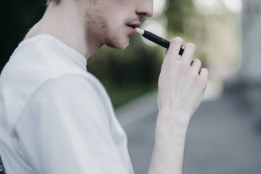  Doğadaki genç bir adam IQOS 'u elinde tutuyor..
