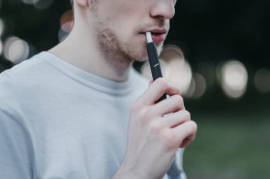  Doğadaki genç bir adam IQOS 'u elinde tutuyor..
