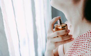 Kadın beyaz arka planda parfüm sürüyor. 