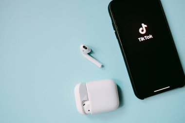 Ekranda TikTok logosu olan iPhone ve AirPodlar, mavi arkaplan.