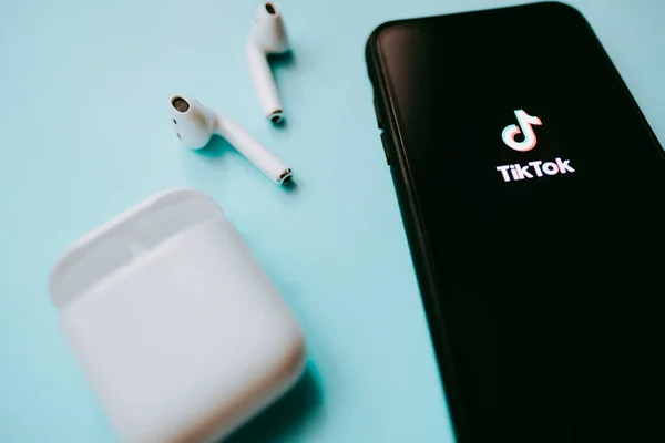 IPhone e AirPods com logotipo TikTok na tela, fundo azul . — Fotografia de Stock