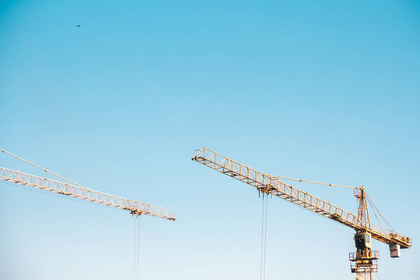 Construction crane tower on blue sky background. Crane and building working progress. Yellow lifting faucet. Empty Space for text. Construction concept. Site. New buildings with a crane.