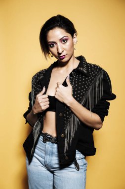 Deri ceket giyen güzel bir kadın portresi ve sarı arka planda güneş gözlüklü kot pantolon.