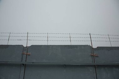 Gri beton bir çitin üzerindeki dikenli tel
