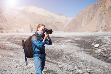 Beautiful woman photographer with backpack on a background of river valley and mountains.