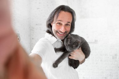 Neşeli yetişkin bir adam, sevgili gri kedisiyle selfie çeker..
