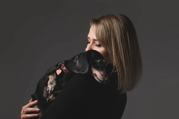 Die schöne Frau hält einen Dackelhund auf dem Arm. Sie umarmen sich. — Stockfoto