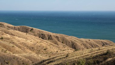 Peyzaj. Güneşli bir günde bozkırdaki kızıl saçlı kayalıkların arasından deniz manzarası.