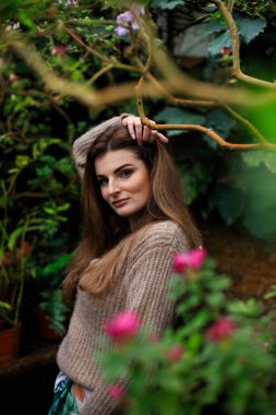 Genç kız botanik bahçesindeki açelyalara hayran. Uzun kahverengi saçlı, süslü elbiseli, çiçekli serada poz veren güzel bir kadın. Açelya çiçekli çekici manken kız.