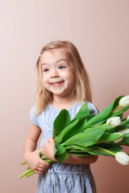 Smiling girl 4 years old posing with a bouquet of white tulips over pink background.