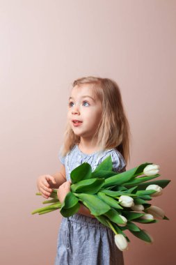 Smiling girl 4 years old posing with a bouquet of white tulips over pink background.
