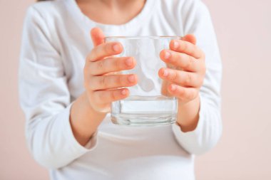 Tarafsız arkaplanda bir bardak su tutan şirin bir cild. Su dengesi kavramı. Bir bardak suyu ellerinle kapat..