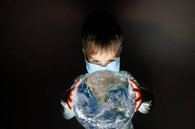 Dünya gezegenini elinde tutan tıbbi maskeli şirin bir çocuk. Bu görüntünün elementleri NASA tarafından desteklenmektedir.